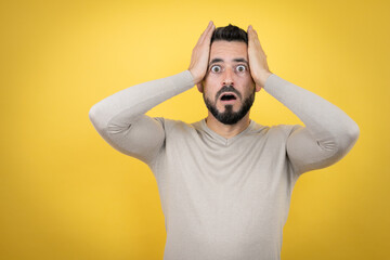 Fototapeta na wymiar Handsome man with beard wearing sweater over yellow background crazy and scared with hands on head, afraid and surprised of shock