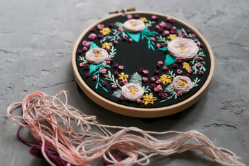 Floral embroidery on a dark convoy and a skein of thread on a gray concrete background 