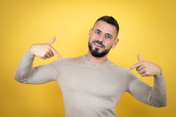 Handsome man with beard wearing sweater over yellow background looking confident with smile on...