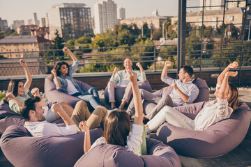 Photo of excited managers sitting beanbags having seminar rising fists urban city terrace outdoors...
