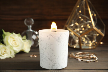 Burning candle and jewelry on wooden table