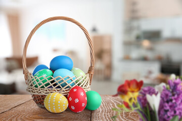 Wicker basket with bright painted Easter eggs on wooden table indoors
