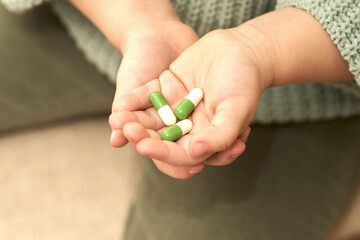 Children's hand with the medication in the capsules is white and green. Close-up. Selective focus. Copy space.