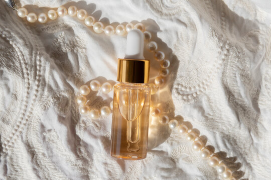 gold beauty serum in a pipette bottle on an ivory fabric