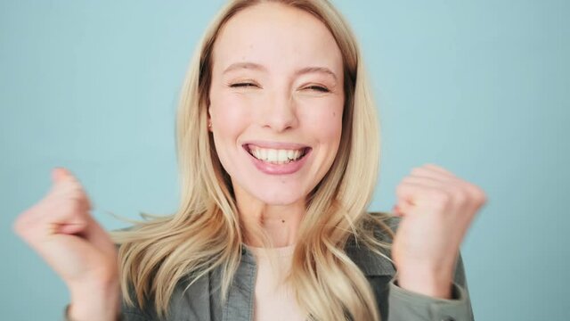 A surprised woman is rejoicing while looking to the camera standing isolated over a blue background in the studio