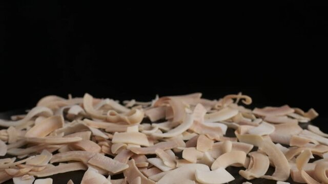 Coconut chips are falling down to the table, close-up, black background. Slow motion