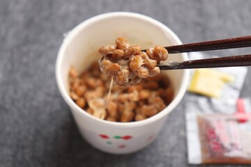 Natto, fermented soybeans in paper cup and close-up of sticky soybeans hold by chopstics