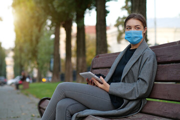 Fototapeta premium Young woman in medical protective face mask holds in hands tablet computer