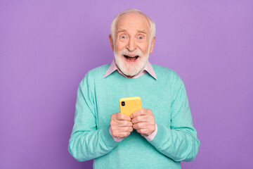 Photo portrait of senior man using cellphone amazed staring cheerfully isolated on pastel violet color background