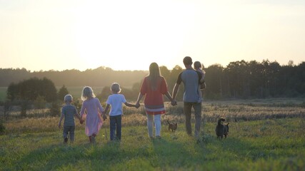 Fototapeta na wymiar A large friendly family walks across the field at sunset with dog.