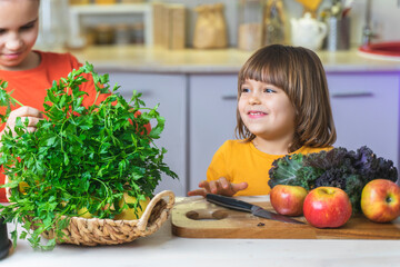 Fun family cooking healthy food. Happy children in the kitchen play and prepare a delicious fresh breakfast of greens, kale, apple, banana, fruit salad, smoothies. Kids hold bouquets of greenery