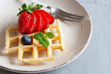 Close-up of soft Viennese waffles on the plate with blueberries, strawberry