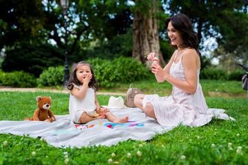 Happy dark haired mother with soap bubble blower having fin with adorable daughter