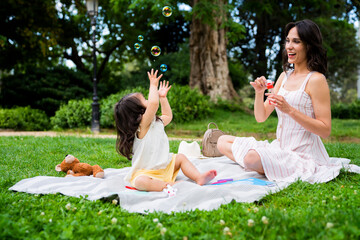 Joyful mommy and daughter playing with bubbles in park