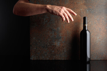 Hand reaches for a bottle of red wine.