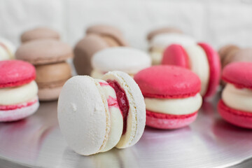 Close up of colorful white, red, and caramel chocolate macarons dessert, filling with tasty ganache, on the table at light kitchen or confectionery shop
