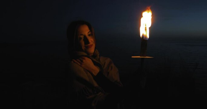 Ragazza con fiaccola di fuoco cammina di notte vicino all'oceano prima del tramonto