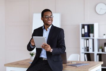 Joyful african american young businessman using digital tablet in office