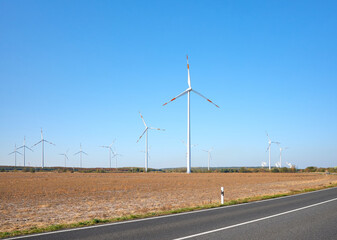 Picture of a wind turbine farm by a road against the blue sky.