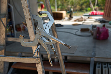 C-Clamp Locking Pliers on the Aluminum Folding Stairs in the Construction Site. 