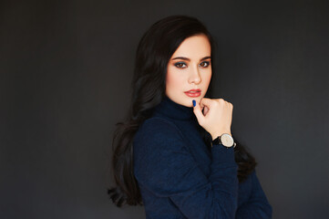 Fashion portrait of pretty young woman wearing turtle neck pullover and watch, posing on dark background