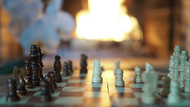 Chess. The hands of a child and an adult move the pieces on the chessboard against the background of the fireplace flame. Close-up shooting.
