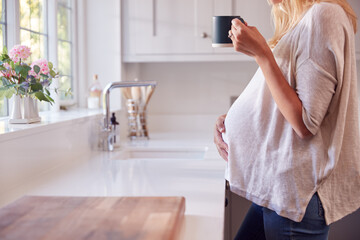 Fototapeta na wymiar Close Up Of Pregnant Woman Standing By Kitchen Window Touching Stomach Relaxing With Hot Drink