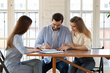 Happy young clients signing paper contract with professional broker or realtor, after discussing...