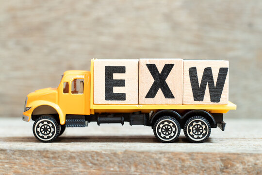 Toy truck hold alphabet letter block in word EXW (abbreviation of Ex works) on wood background