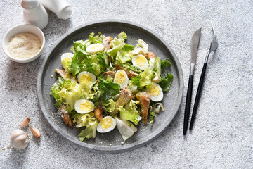 Traditional caesar salad with grilled chicken and parmesan on a concrete plate.