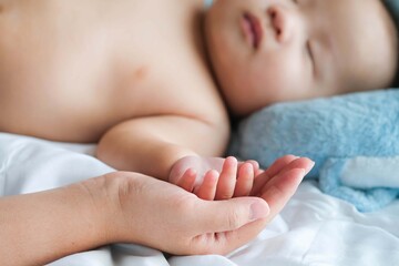 Selective focus hand of sleeping baby in the hand of mother close up on the bed, New family and baby protection from mom concept