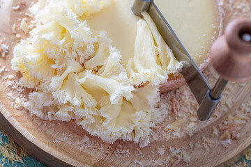 Top view of round Swiss cheese Monk head on a wooden round board and a special metal knife. Soft focus. Close-up