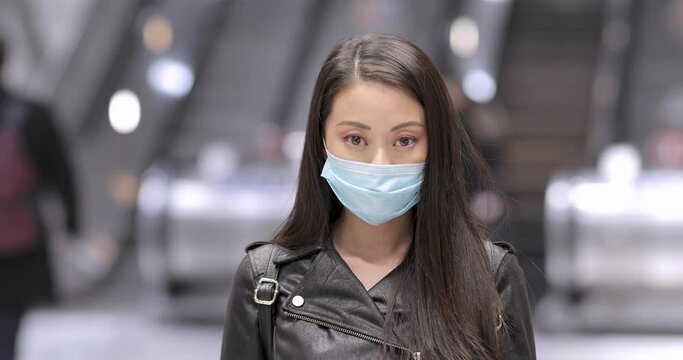 Chinese woman in London wearing face mask to protect from covid 19 coronavirus - young asian woman portrait in a busy public place protecting from virus - health and lifestyle