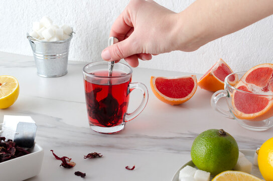 Woman stiring sugar in the tea cup.Fresh lemon, lime and grapefruit, herbal tea leaves on the white table