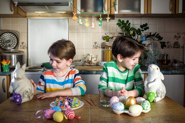 Fototapeta premium Two little kid boy coloring eggs for Easter holiday in domestic kitchen, indoors. Sibling brothers having fun and celebrating feast