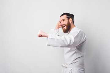 Young bearded man wearing taekwondo uniform punching over white background.