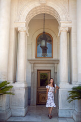 woman in a white dress with flowers stands at the entrance of the door to the castle with columns