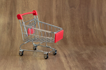 Small miniature supermarket trolley on dark wooden background, close up with empty space