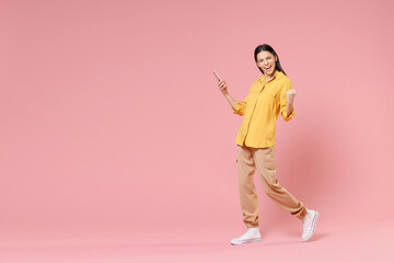Fototapeta na wymiar Full length side view of young brunette nice attractive latin woman 20s wearing yellow shirt hold mobile cell phone do winner gesture clench fist isolated on pastel pink background studio portrait.