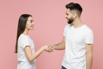Fototapeta premium Young cheerful couple two friends man woman in white basic blank t-shirts hold hand folded handshake gesture isolated on pastel pink color background studio portrait Friendship business greet concept