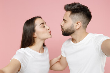 Obraz premium Close up young cheerful couple two friends man brunette woman in white basic blank print design t-shirt doing selfie shot on mobile cell phone isolated on pastel pink color background studio portrait