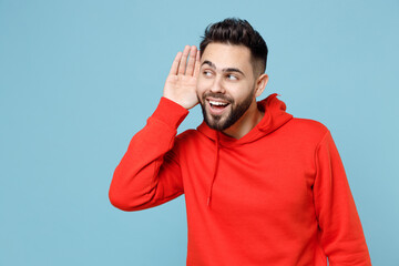 Young caucasian bearded curious attractive man 20s in casual red orange hoodie try to hear you...