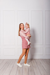 Fototapeta na wymiar Thirty-year-old happy woman holds a one-and-a-half-year-old girl in her arms. pink corduroy sundresses