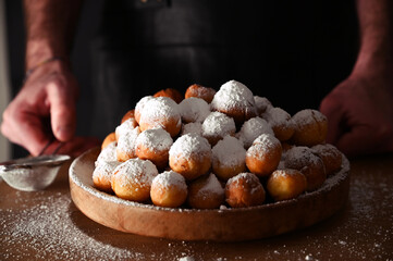 Man sprinkles powdered sugar onBaked castagnole. Round biscuits with sugar for the carnival of Venice. Traditional sweet pastries during the carnival period in italy. horizontal photo. Copy space. 
