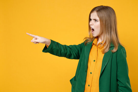 Little blonde kid angry strict girl 12-13 years old in casual clothes green shirt point index finger aside screm shout isolated on yellow orange background children studio portrait Childhood concept.