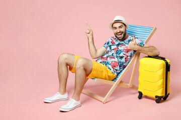 Full length of funny traveler tourist man in summer clothes hat sit on deck chair point finger up...