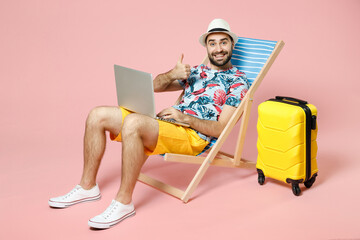Full length smiling young traveler tourist man in hat sit on deck chair work on laptop computer...