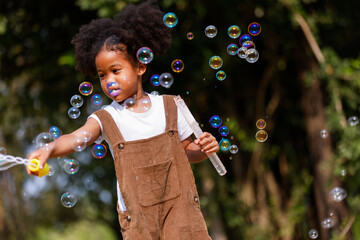 Little African American curly hair girl in casual clothing holding bubble wand blowing bubbles...
