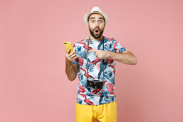 Shocked traveler tourist man in summer clothes, hat point index finger on mobile cell phone typing sms message isolated on pink background. Passenger traveling on weekends. Air flight journey concept.