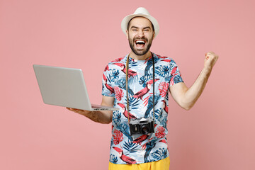 Happy traveler tourist man in summer clothes hat working on laptop computer booking hotel doing winner gesture isolated on pink background. Passenger traveling on weekends. Air flight journey concept.